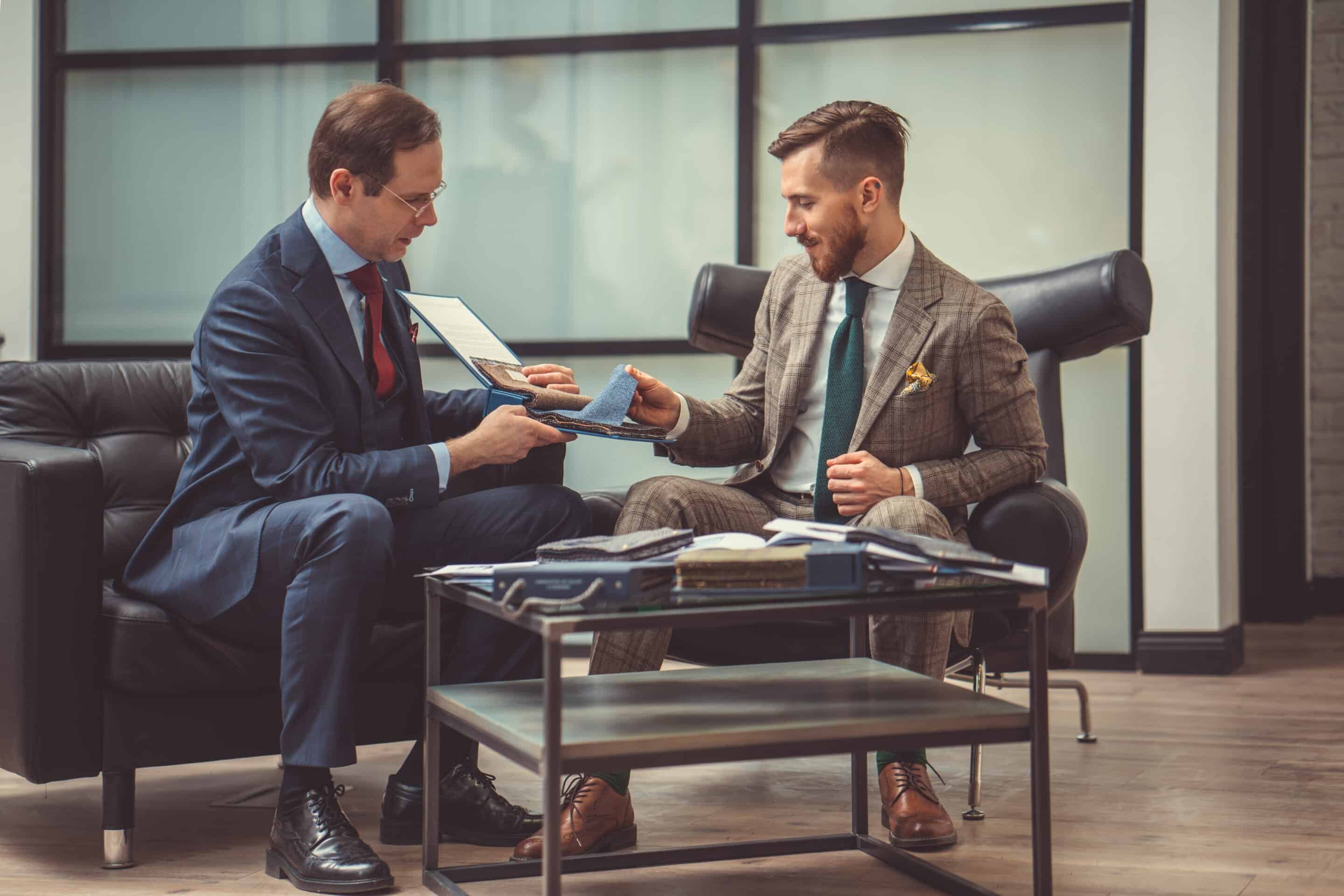 Hommes en costumes discutent de tissus dans un bureau.